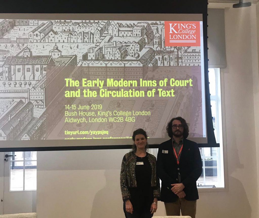 Photo of the Conference organisers Romola and Julian in front of a presentation screen looking happy and welcoming
